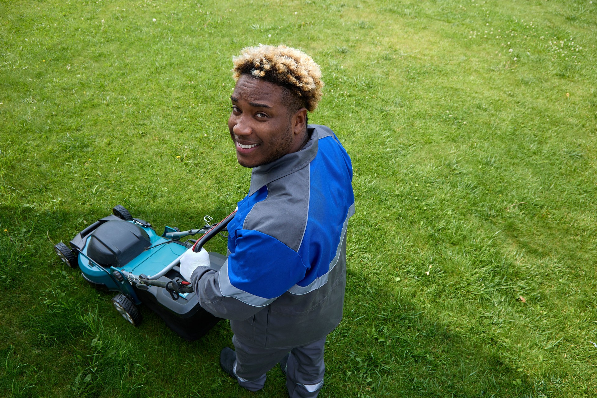 Black man looks up and smiles using a lawn mower in the backyard.